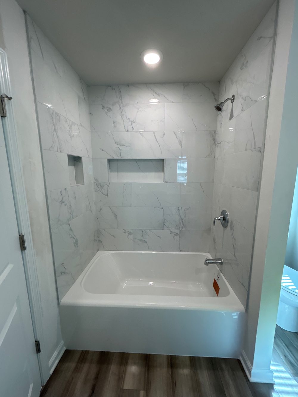 After: a new white tub with marble-look tile on three walls up to the ceiling, a long horizontal niche on the back wall and a second niche on the side wall