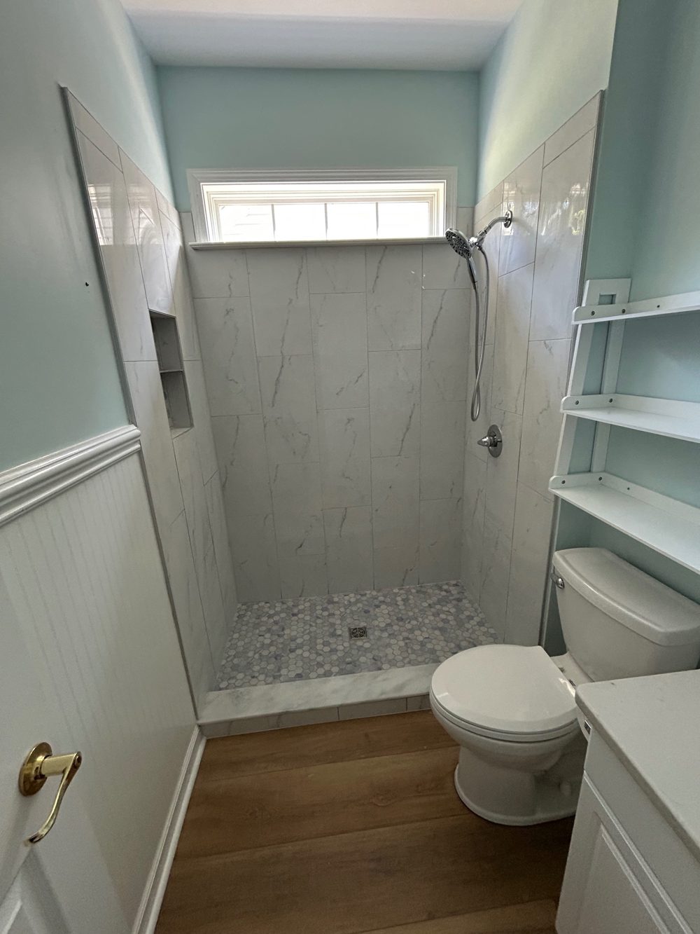 After: a walk-in shower with large marble-look wall tile, a built-in niche, a hexagon mosaic floor and a handheld shower head