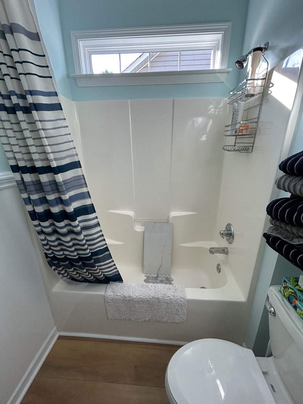 Before: a fiberglass tub and shower surround with a striped curtain, tile samples resting in the tub